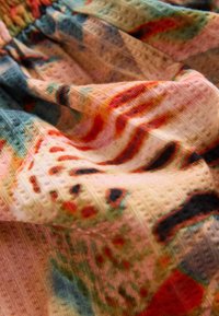 Telas textiles en colores vibrantes, con patrones intrincados en rojo, verde y azul sobre una superficie suave y texturizada con un sutil brillo.