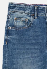 Džínsy z denimu s svetlomodrým umývaním, klasickým dizajnom s piatimi vreckami a oranžovým prešívaním. Malý srdiečkový detail na prednom vrecku.