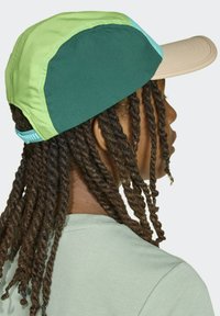 Czapka ma wielokolorowy wzór z panelami w kolorze zielonym, jasnoniebieskim i beżowym, zakrzywiony daszek oraz teksturowany materiał. Zawiera regulowany pasek.
