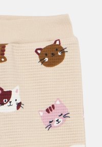 Tela beige con estampado de caras de gatos ilustradas en marrón, blanco y rosa, con una superficie texturizada y una cintura acanalada.