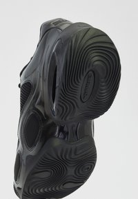 Semelle de chaussure de sport noire avec motif ondulé texturé et unité d'amorti à air visible dans la semelle intermédiaire sur un fond clair.