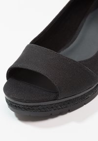 Chaussure plate noire à bout ouvert avec dessus en tissu texturé, détail de semelle intermédiaire tissée et semelle extérieure en caoutchouc, vue en gros plan.