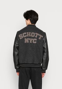 Black leather-sleeved varsity jacket with gray wool body. Features “SCHOTT NYC” in beige embroidery on back, ribbed hem, and cuffs.