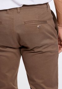 Braune Baumwollhosen mit einer Gesäßtasche mit Druckknopfverschluss und einer glatten Textur. Das Design umfasst Gürtelschlaufen und eine taillierte Passform.