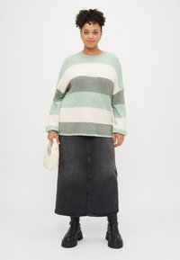 Svetlozeleno in sivo prugasto pulover, sproščenega kroja, z dolgimi rokavi. Kombiniran s temno denim maksi krilom in črnimi čevlji do kolen.