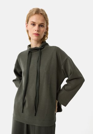 Ciemnozielony, oversize'owy sweatshirt z wysoką kołnierzem, sznurkiem i szerokimi rękawami. Miękka tekstura i luźny krój.