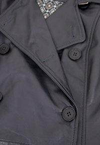 Schwarzer, doppelt geknöpfter Ledermantel mit großen Knöpfen, Reverskragen und subtiler Textur. Verfügt über einen gemusterten Stoff, der von innen hervorschaut.