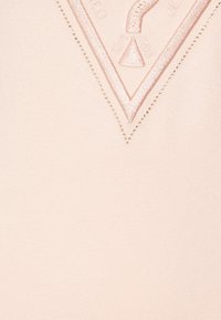 Jasnoróżowy materiał z teksturowanym wykończeniem ma wyszywany trójkątny wzór oraz małe metaliczne akcenty wzdłuż krawędzi.