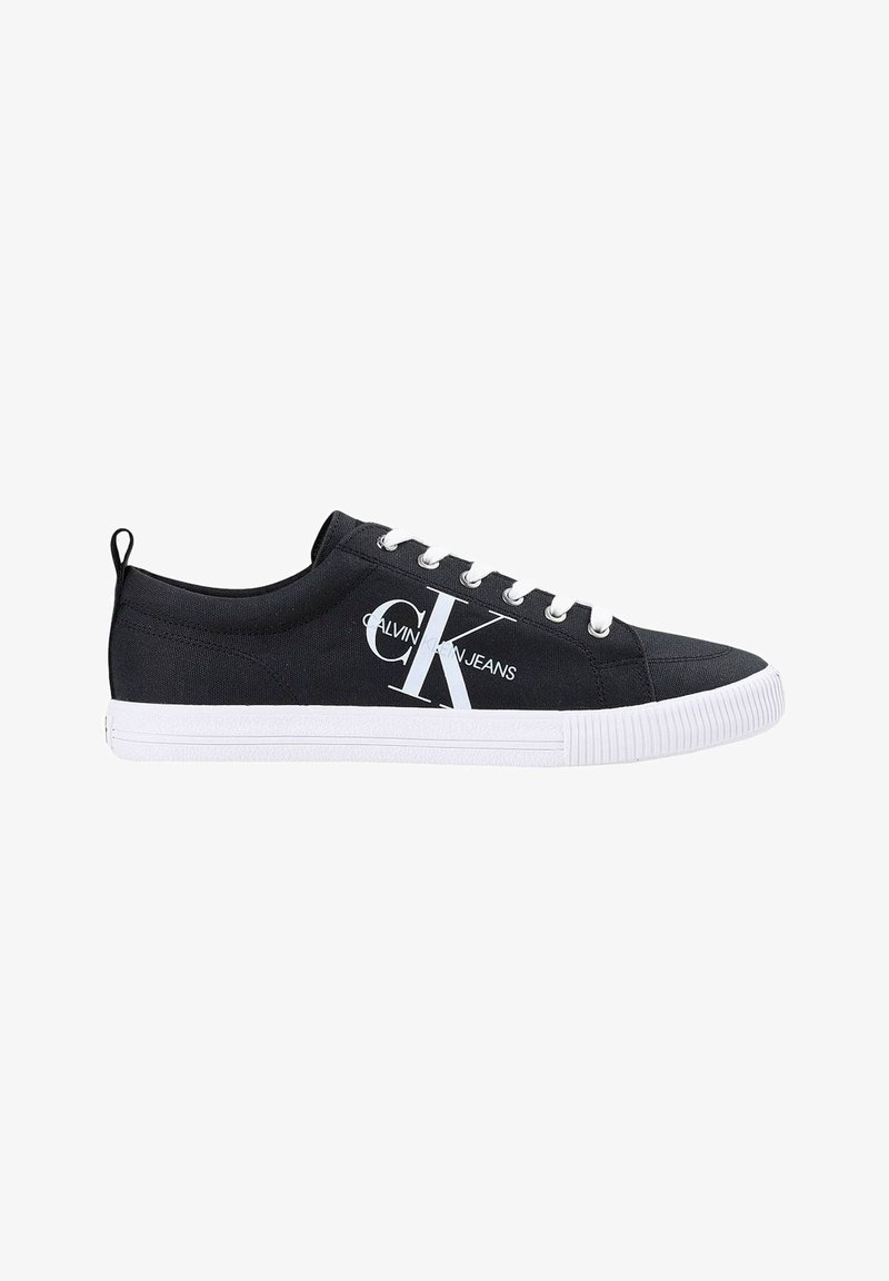 Baskets basses en toile noire avec lacets blancs, semelle en caoutchouc blanche et grand logo Calvin Klein Jeans sur le côté.