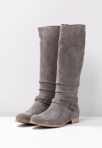 Botas de ante gris hasta la rodilla con un diseño arrugado, que cuentan con detalles de correas y un tacón bajo. Textura suave y forma de punta redonda.