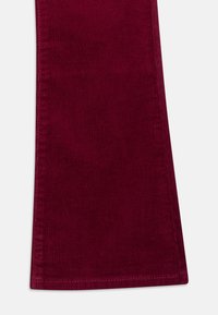 Lähikuva viininpunaisista corduroy-housuista, joka näyttää kankaan tekstuurin ja ompelun helman kohdalla.