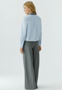 Hellblaue Bluse mit Streifen und grauem Kragen, kombiniert mit hochgeschnittenen grauen Hosen mit weitem Bein. Das Modell ist von hinten zu sehen.