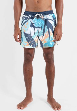 Buste et jambes masculins portant un short de bain bleu, orange et blanc à motif de feuilles tropicales avec une ceinture bleu marine et un cordon blanc.