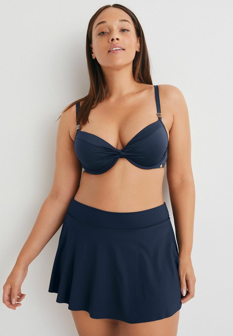 Mornarsko modra bikini spodnja majica z oblogo in zvitim detajlom, v kombinaciji z ujemajočo se razširjeno kopalno krilo. Gladka tkanina, nastavljivi trakovi, minimalna oprema.