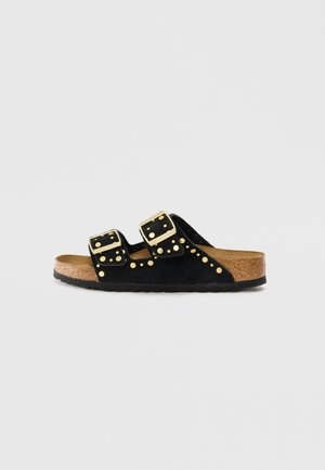 Sandália em camurça preta com duas tiras ajustáveis em fivela dourada, tachas decorativas em dourado e uma palmilha de cortiça texturizada.