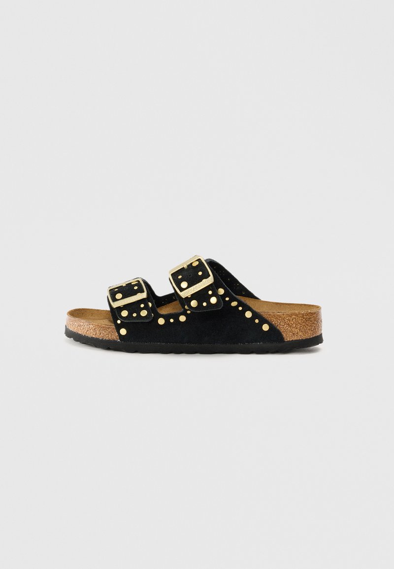 Sandale à glissière en suede noir avec deux sangles ajustables en or, des clous décoratifs dorés et une semelle en liège texturée.