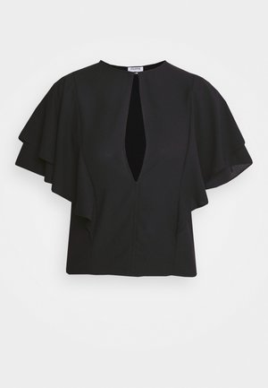 Musta asu, joka sisältää liehukä sleeves -yöpaitan etuosan avonaisella yksityiskohdalla, yhdistettynä leveälahkeisiin housuihin ja litteisiin mustiin sandaaleihin. Rakenne taustalla.