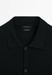 Polo en coton noir avec deux boutons, col ouvert et étiquette de marque à l’intérieur du col.