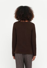 Braunes geripptes Langarmshirt mit rundem Ausschnitt, taillierter Silhouette und strukturiertem Stoff, kombiniert mit grauen strukturierten Hosen.