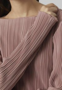 Růžový top s dlouhými rukávy z plisované látky s jemnými vertikálními pruhy, s širokým výstřihem a texturovaným detailem na rukávech.
