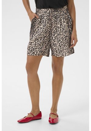 Shorts en imprimé léopard en tissu léger avec une taille élastique, dotés de poches latérales ; associés à des chaussures plates rouges.