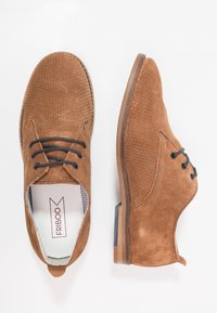 Hnědé semišové boty s perforovaným designem, kulatou špičkou, černými šněrováním a malým podpatkem. Interiér má pruhované podšívku.