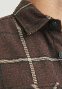 Bruin geruite flanellen shirt met een kraag, met beige en donkerblauwe lijnen, en zwarte knopen. Zachte textuur met een geruit patroon.