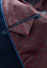 Tumeda sinelõngast väliskangas tumesinisena, marooni voodriga, millel on sinise ja beeži paisleimuster, mida täiendavad sinised äärised.