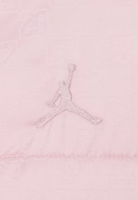 Jasnoróżowy materiał z wytłaczanym wzorem "23" oraz białym logo Jumpman. Materiał wydaje się gładki o miękkiej fakturze.