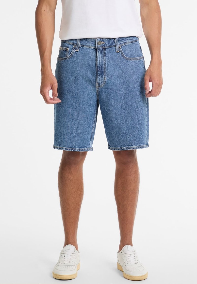 Shorts de denim en azul claro, con un diseño clásico de cinco bolsillos, trabillas para cinturón y dobladillo cosido, combinados con zapatillas blancas.