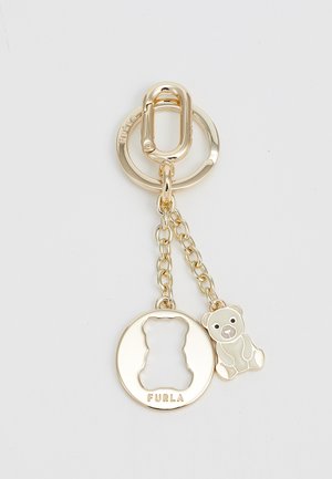 Llave de oro con un silueta en forma de oso, un charm de oso y una cadena, con "FURLA" grabado en el círculo.