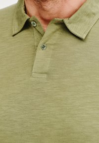 Oliwkowa koszulka polo o miękkiej fakturze, klasycznym kołnierzyku i dwóch guzikach przy szyi. Subtelny poziomy wzór dzianiny.