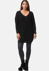 Schwarzer Strickpullover mit V-Ausschnitt, langen Ärmeln und lockerer Passform. Kombiniert mit dunklen Skinny Jeans und schwarzen High-Heels.