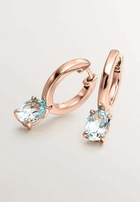 Pendientes de aro en oro rosa con cristales ovalados de color azul claro, destacando metal pulido y engastes de seis garras, textura suave y diseño elegante.