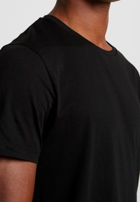 T-shirt en coton noir avec un col rond classique. Le tissu est lisse et légèrement extensible, mettant en valeur une coupe ajustée.