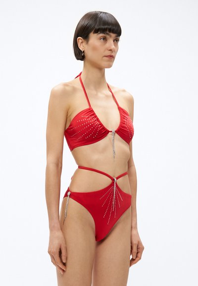 Červené bikiny s viazaním za krk, zdobené nitmi a bočnými remienkami, doplnené kovovými detailmi a priliehavým strihom.