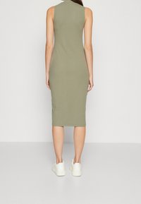 Robe midi sans manches, côtelée, vert olive avec un col haut, une coupe ajustée et des fentes latérales, associée à des baskets blanches.