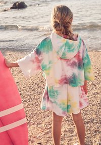 Tie-dye strandcoverup i blødt fleece-stof med hætte, korte ærmer og en farverig blanding af pastelfarver; kombineret med et pink surfbræt.