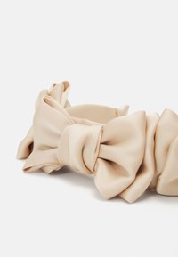 Fascia per capelli in satin beige caratterizzata da un ampio design a fiocco annodato con una texture morbida e fluida e una finitura liscia.