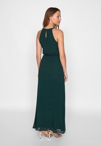 Μακρύ, σκούρο πράσινο φόρεμα από ρέον ύφασμα, με ψηλή λαιμόκοψη, άνοιγμα στο πίσω μέρος και ελαστική μέση με φουσκωτή φούστα.