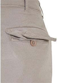 Krémové kalhoty s kapsou na klopu zabezpečenou hnědým knoflíkem. Mají hladký povrch a šité detaily na pase a kapse.