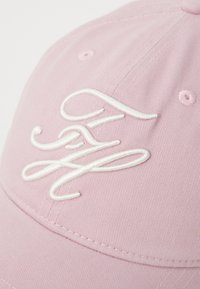 Căciulă roz dintr-un material texturat, având un logo alb brodat în față. Designul include accente cusute și o bordură curbată.