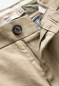 Beige Slim-Fit-Hosen mit einem Knopf- und Reißverschluss, ausgestattet mit einem gemusterten Innenfutter und einem strukturierten Baumwollstoff.