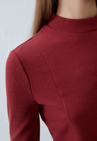 Burgundi színű, bordázott garbós pulóver, formázott szabással, sima textúrával és finom varrásokkal a vállnál.