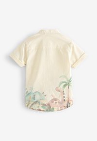 Chemise pour enfant à manches courtes couleur crème avec poignets retroussés et motifs peints de dinosaures et de palmiers sur le bas du dos.