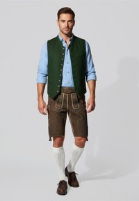 Groene vest over een blauw geruit shirt, bruine kniebovenlange shorts met bloemmotieven, witte gebreide sokken en bruine schoenen.