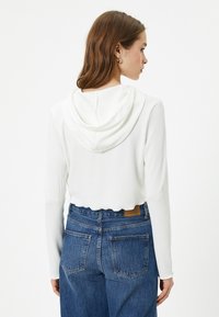 Witte geribbelde cropped hoodie met een trekkoord in de capuchon, gecombineerd met hoge taille blauwe denim jeans met een label en subtiele details op de achterzak.