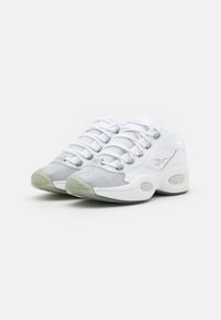 White athletic sneakers with grey patent accents, mesh panels, and rounded toe. Features flat laces and circular rubber soles.