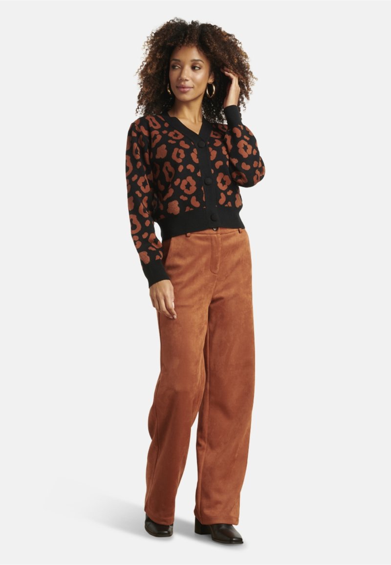 Black cardigan with orange leopard spots, ribbed cuffs, and solid waistband; paired with rust-colored wide-leg pants and black heeled boots.