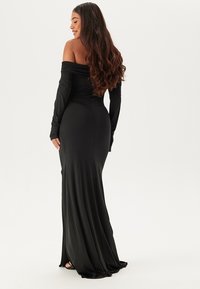 Svart, off-the-shoulder klänning med långa ärmar, figurnära design, slät textur och flödande nederkant, med en subtil lyster.